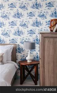 AUG 4, 2014 Hua Hin, THAILAND - Vintage cozy hotel room with bed, white ceramic lamp, pillows, blue pattern wallpaper, wooden side table and cabinet. Vintage country home decoration
