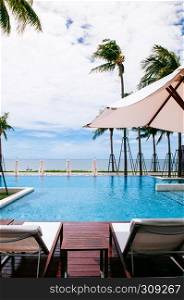 AUG 6, 2014 Hua Hin, Thailand - Tropical seaside resort style infinity edge pool with beach bed under white umbrella and coconut trees in summer