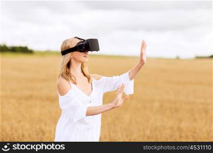 augmented reality, gaming, summer holidays, technology and people concept - happy young woman with virtual reality headset or 3d glasses on cereal field touching something