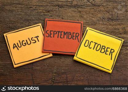 August, September and October - handwriting in black ink on sticky notes against rustic wood
