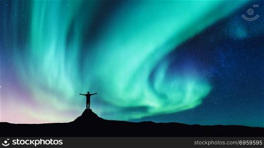 Aurora and silhouette of standing man on the stone. Aurora and silhouette of standing man on the stone with raised up arms in Norway. Aurora borealis and happy man. Starry sky, green polar lights. Night landscape. Northern lights. Travel and tourism