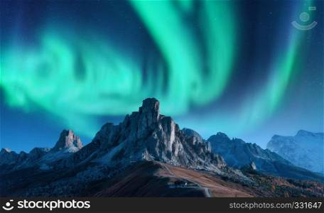 Aurora borealis above mountains at night in Europe. Northern lights. Sky with stars with polar lights and high rocks. Beautiful landscape with aurora, buildings on the hill, mountain ridge. Travel