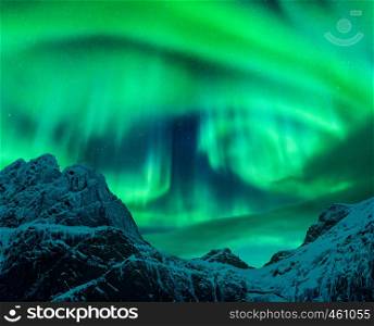 Aurora borealis above the snow covered mountain peak in Lofoten islands, Norway. Northern lights in winter. Night landscape with polar lights, snowy rocks. Starry sky with aurora. Nature background
