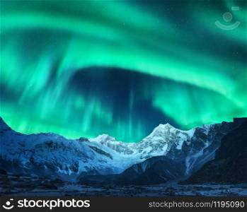 Aurora borealis above the snow covered mountain peak in Norway. Northern lights in winter. Night landscape with green polar lights and snowy mountains. Starry sky with aurora over the rocks. Space