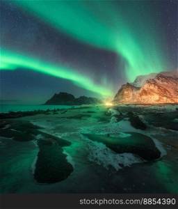 Aurora borealis above Uttakleiv beach in Lofoten islands, Norway. Beautiful northern lights in winter. Starry sky with polar lights. Night landscape with aurora, sea coast, stones, snowy mountains