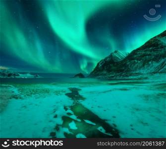 Aurora borealis over snowy mountains, frozen sea coast and reflection in ice at night in Lofoten islands, Norway. Northern lights. Winter landscape with polar lights, beach in snow, starry sky, aurora