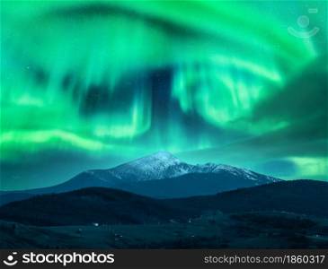 Aurora borealis over the snow covered mountain peak in europe. Northern lights in winter. Night landscape with green polar lights and snowy mountains and hills. Starry sky with aurora. Nature. Space