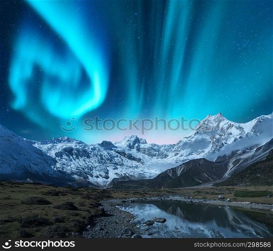 Aurora borealis over the snowy mountains, coast of the lake and reflection in water. Northern lights above snow covered rocks. Winter landscape with polar lights, lake. Starry sky with green aurora