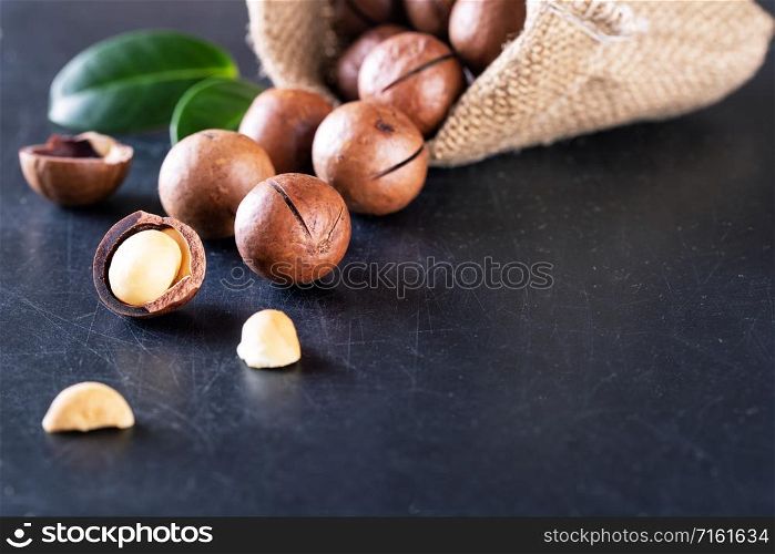 Australian macadamia nuts with green leaves spilled out of the bag against a black background