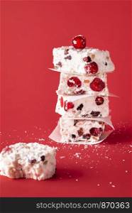 Australian Xmas traditional dessert, a white Christmas cakes, piled in a stack and an eaten piece, on a red background. Winter holidays festive sweets