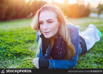 Authentic portrait of a pretty girl lying down on fresh green grass meadow, genuine beauty of a young woman, enjoying spring nature and peaceful weekend in countryside . Pretty girl lying down on green grass