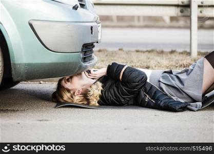Auto assistance and insurance, troubles while traveling concept. Woman trying to repair her broken car, checking what is under automobile.. Woman, repairing broken car lying under it