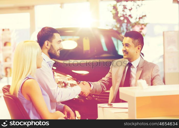 auto business, car sale, and people concept - happy couple with dealer shaking hands in auto show or salon