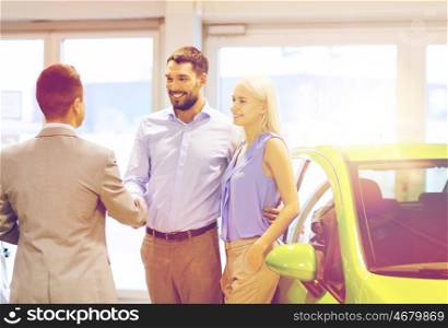 auto business, car sale and people concept - happy couple with dealer shaking hands in auto show or salon