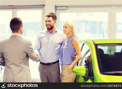 auto business, car sale and people concept - happy couple with dealer shaking hands in auto show or salon
