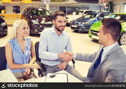 auto business, car sale, and people concept - happy couple with dealer shaking hands in auto show or salon