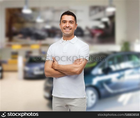 auto business, car sale and people concept - smiling man in white t-shirt with crossed arms over auto show background