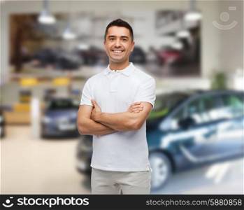 auto business, car sale and people concept - smiling man in white t-shirt with crossed arms over auto show background