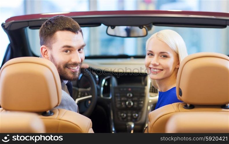 auto business, car sale, consumerism and people concept - happy couple sitting in car at auto show or salon