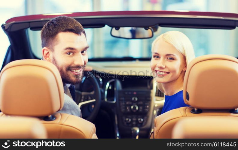 auto business, car sale, consumerism and people concept - happy couple sitting in car at auto show or salon