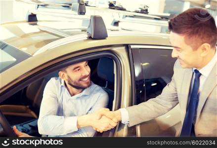 auto business, car sale, consumerism, gesture and people concept - happy man with car dealer making deal and shaking hands in auto show or salon