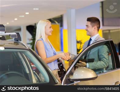 auto business, car sale, consumerism, gesture and people concept - happy woman with car dealer making deal and shaking hands in auto show or salon