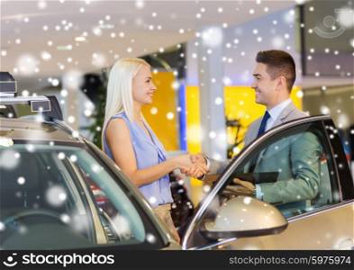 auto business, car sale, consumerism, gesture and people concept - happy woman with car dealer making deal and shaking hands in auto show or salon over snow effect