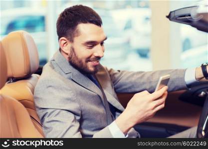 auto business, car sale, consumerism, technology and people concept - happy man sitting in car with smartphone at auto show or salon