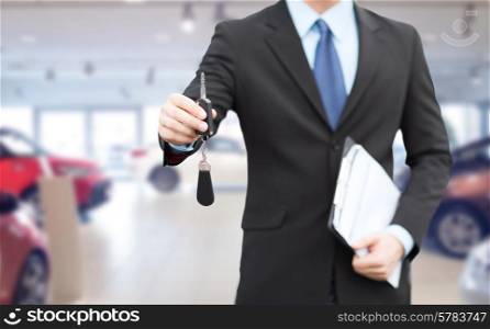 auto business, car sale, gesture and people concept - close up of businessman or salesman with documents giving car key over auto show background