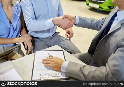 auto business, car sale, gesture and people concept - close up of customers couple with dealer shaking hands in auto show or salon