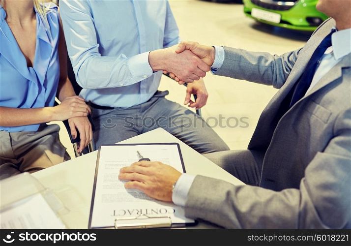 auto business, car sale, gesture and people concept - close up of customers couple with dealer shaking hands in auto show or salon