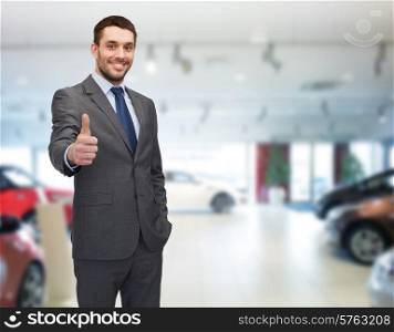 auto business, car sale, gesture and people concept - smiling businessman showing thumbs up over auto show background