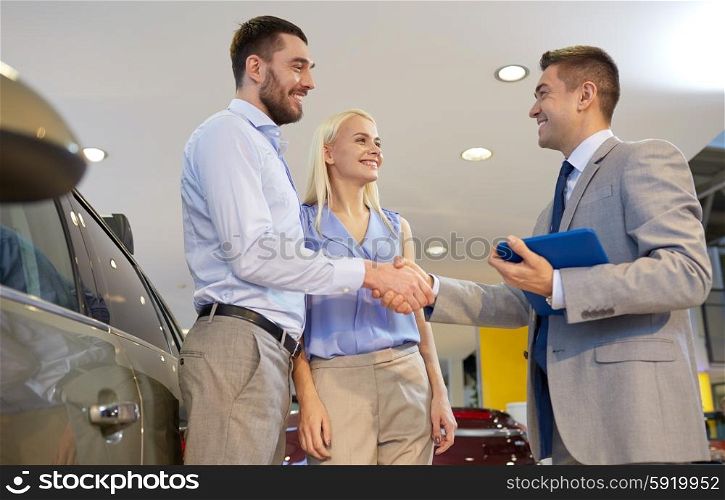 auto business, car sale, technology, gesture and people concept - happy couple with car dealer shaking hands in auto show or salon