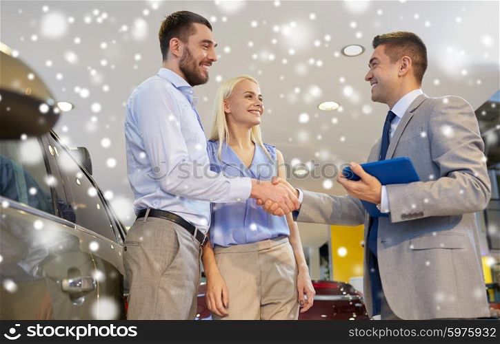 auto business, car sale, technology, gesture and people concept - happy couple with car dealer shaking hands in auto show or salon over snow effect