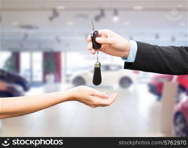 auto business, car sale, transportation, people and ownership concept - close up of car salesman giving key to new owner or customer over auto show background