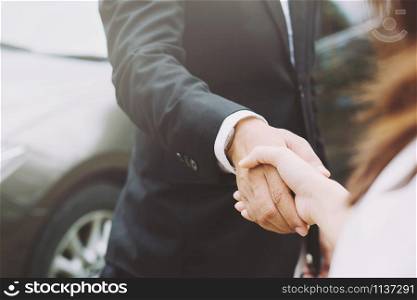 auto business. Close up of a business man salesman dealer offer car to new owner and hand shake female between two congratulations to customers.
