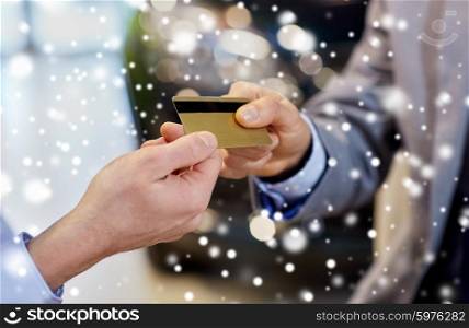 auto business, sale and people concept - close up of customer hand giving credit card to car dealer in auto show or salon over snow effect