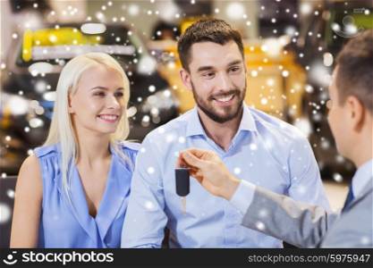 auto business, sale and people concept - happy couple with dealer giving car key in auto show or salon over snow effect