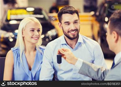 auto business, sale and people concept - happy couple with dealer giving car key in auto show or salon