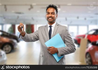 auto business, sale and people concept - happy indian car dealer showing key over showroom background. happy indian car dealer with car key at showroom