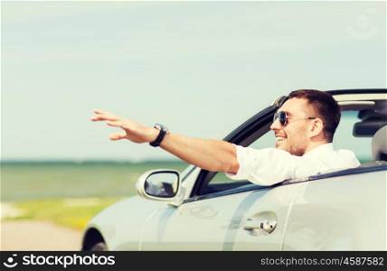 auto business, transport, leisure and people concept - happy man driving cabriolet car and waving hand outdoors