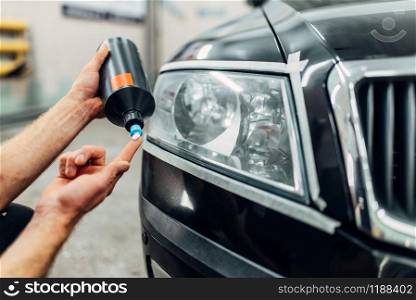 Auto detailing of car headlights on carwash service. Man smears polishing paste. Detailing of headlight, man smears polishing paste