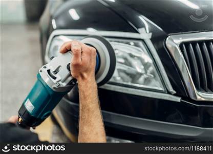 Auto detailing of car headlights on carwash service. Man works with polishing machine. Detailing of car headlights with polishing machine