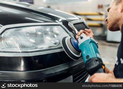 Auto detailing of car headlights on carwash service. Worker cleaning glass with polishing machine. Auto detailing, worker with polishing machine