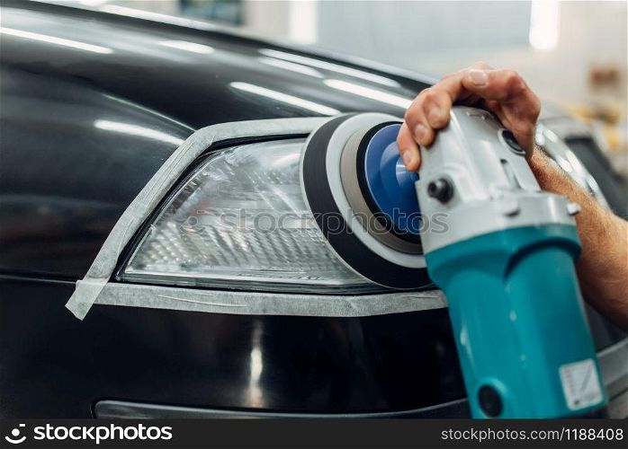 Auto detailing of car headlights on carwash service. Worker cleaning glass with polishing machine. Auto detailing, worker with polishing machine