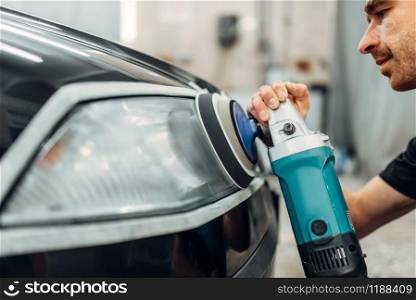 Auto detailing of car headlights on carwash service. Worker cleans glass with polishing machine