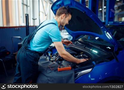 Auto electrician in uniform checks electrical circuits on car service station. Automobile checking and inspection, professional diagnostics and repair. Auto electrician checks electrical circuits