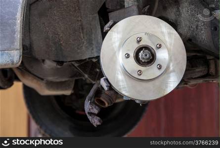 Auto in service. Front disk brake on car in process of damaged tyre replacement. Closeup detail of the wheel assembly on automobile.