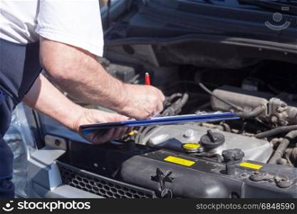 Auto mechanic checking car engine and writing on the clipboard. Car or auto mechanic checking a car engine and writing on the cl