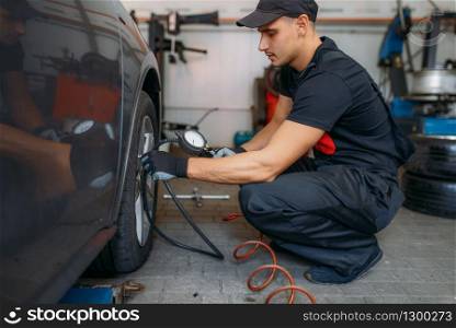 Auto mechanic checks the tire pressure in repairing service. Man repairs car tyre in garage, professional automobile inspection in workshop